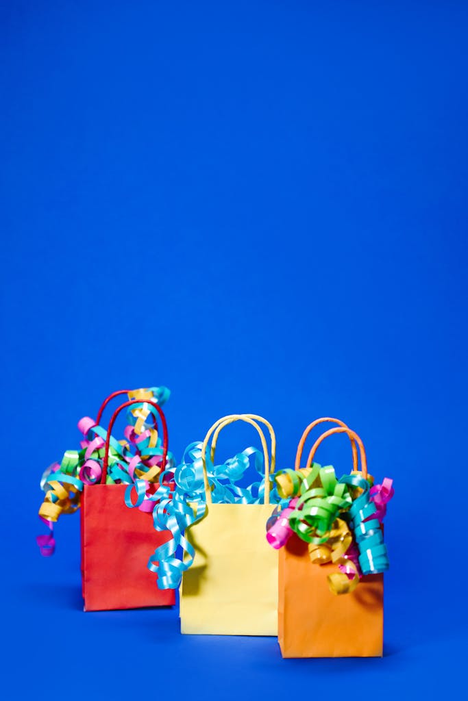 Three colorful paper gift bags with ribbons set against a blue background. Perfect for celebration themes.