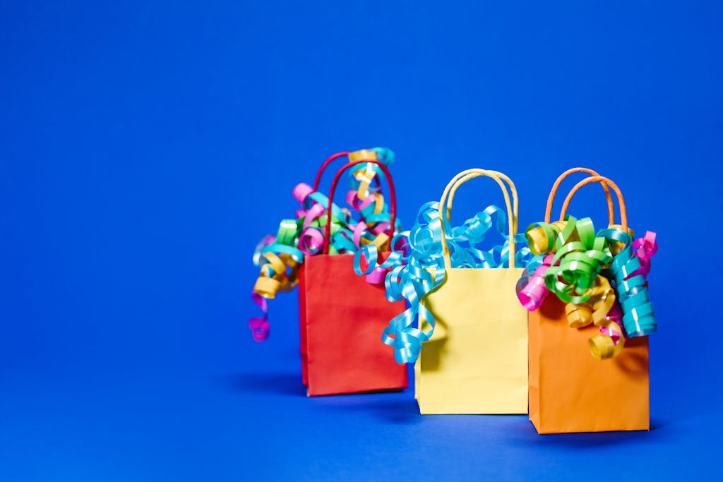 Vibrant paper gift bags with curly ribbons against a solid blue background.